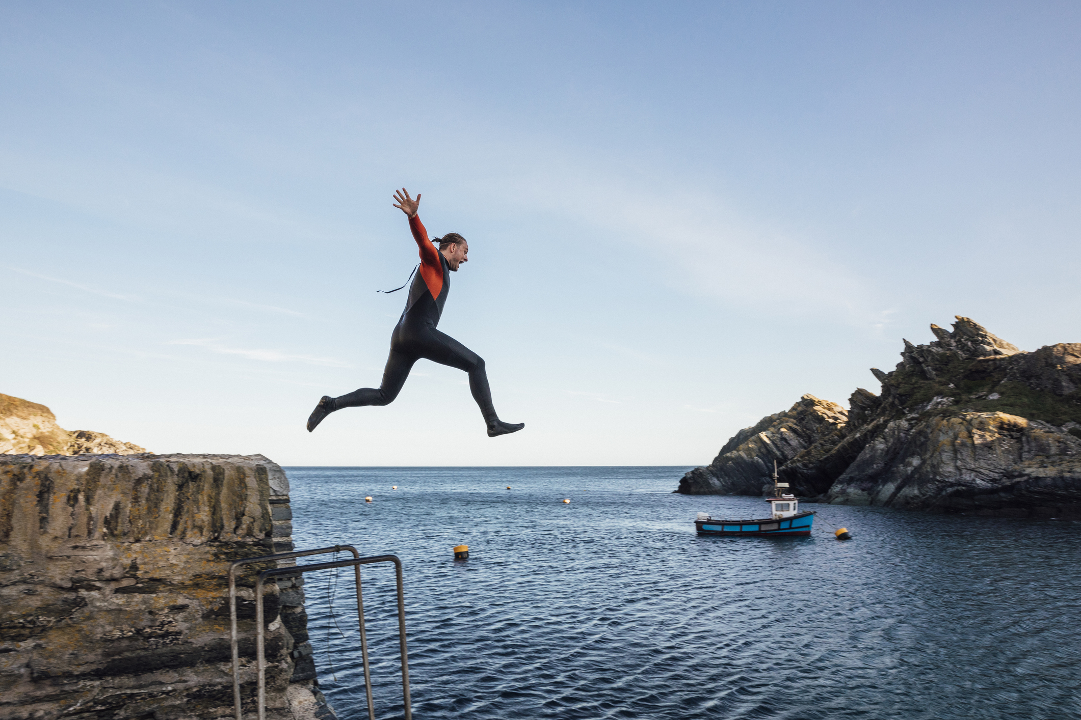 A man in a wet suit is mid-air, jumping from a ledge into the sea demonstrating stepping outside your comfort zone to boost confidence.