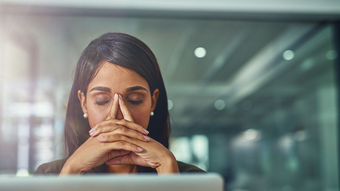 Woman looks tired or annoyed with clasped hands over her chin and closed eyes.