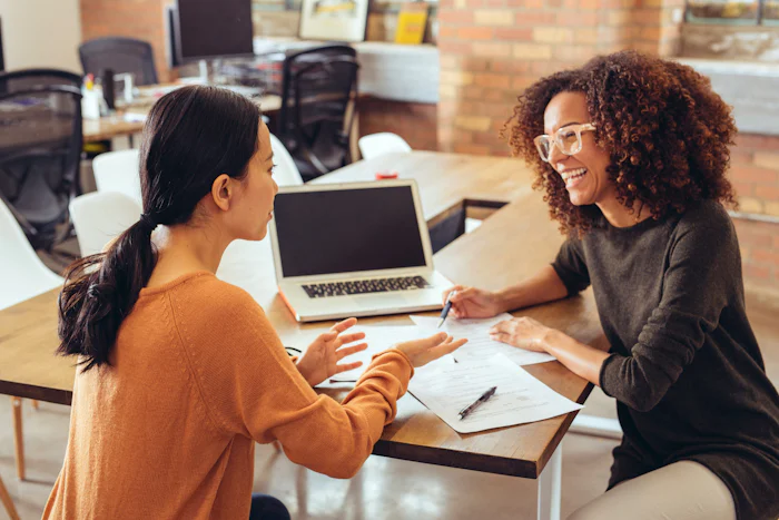 Two female colleagues discussing something in a work environment, representing feedback