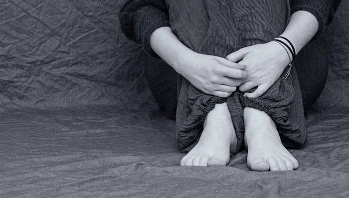 Barefoot human crouched hugging knees