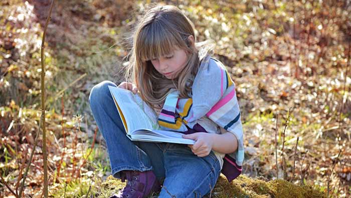 Young girl reading a book in the woods