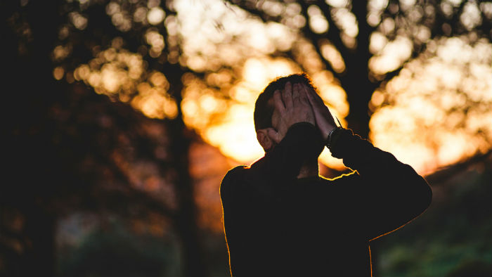 A man standing outside with his hands over his face.