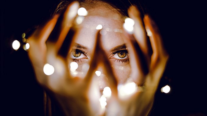 A woman holding fairy lights in her hands in front of her face.