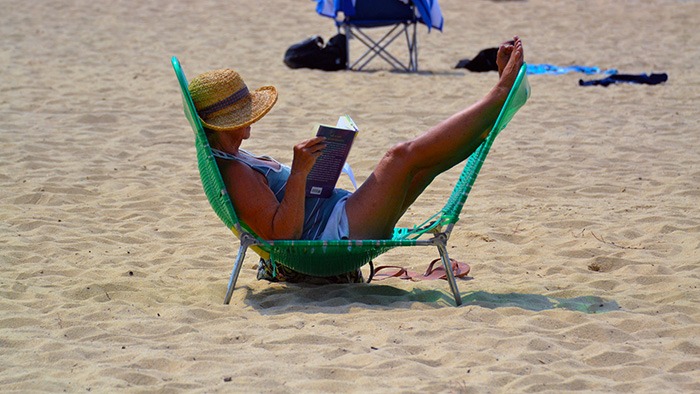 Woman reads in lounger with feet up on beach