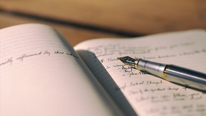 Fountain pen lying on the open pages of a notebook with writing on the page