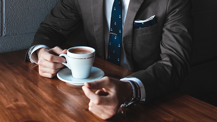 Man in suit drinks cup of coffee at a table