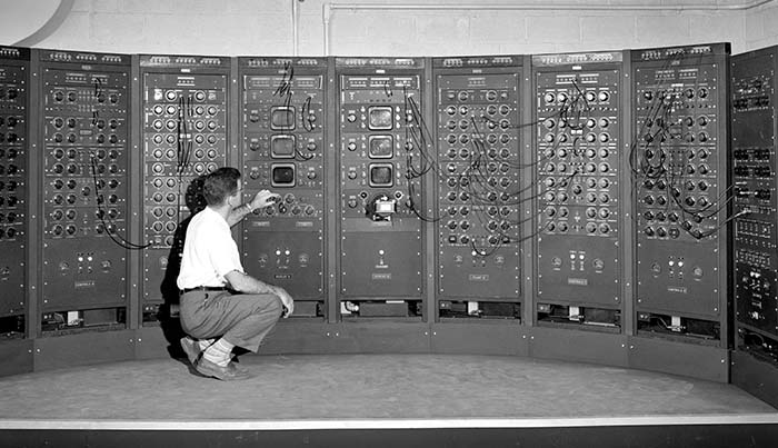 Man crouching by a very early computer