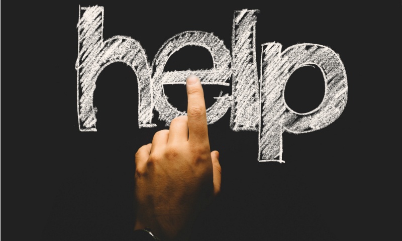 A finger pointing at the word "help" written in white chalk.