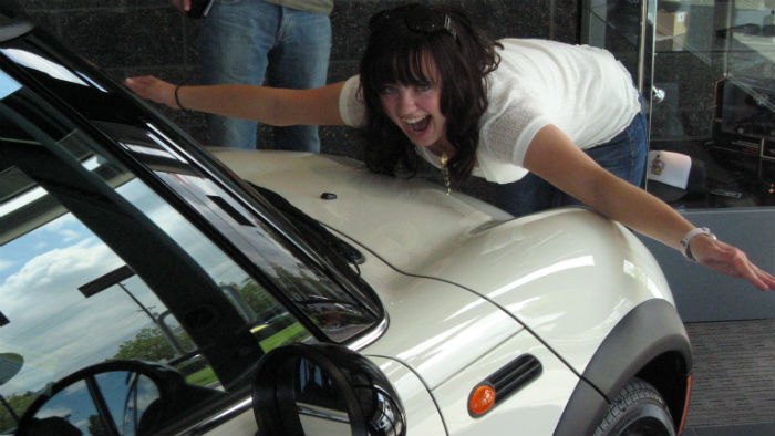 A girl posing next to a white car.